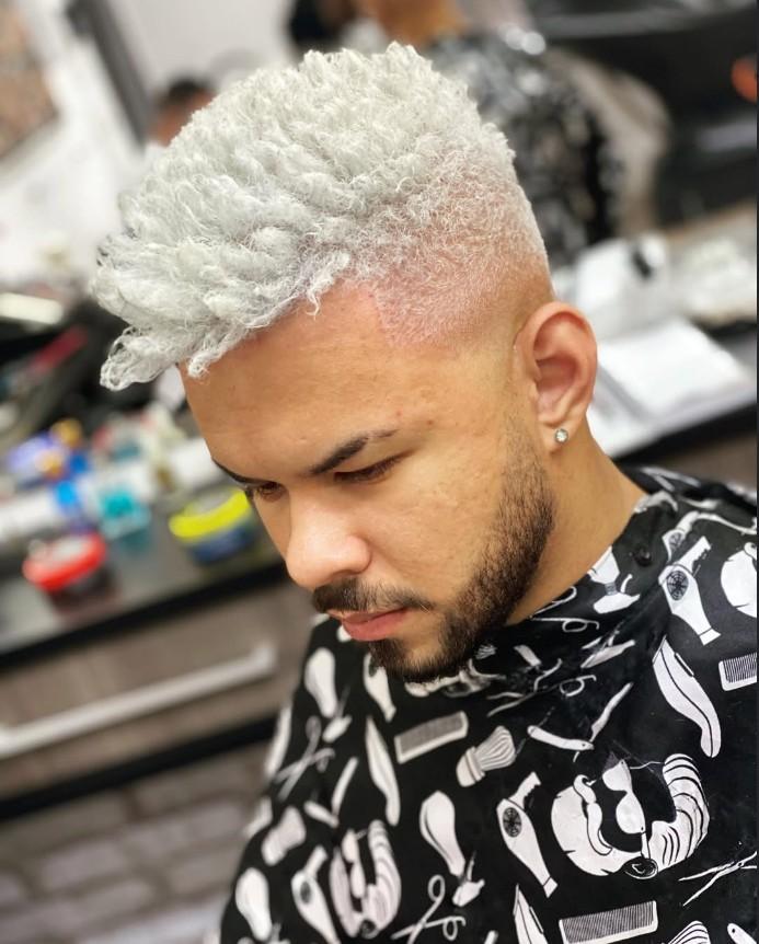 Homem de perfil com cabelo crespo platinado e degradê nas laterais